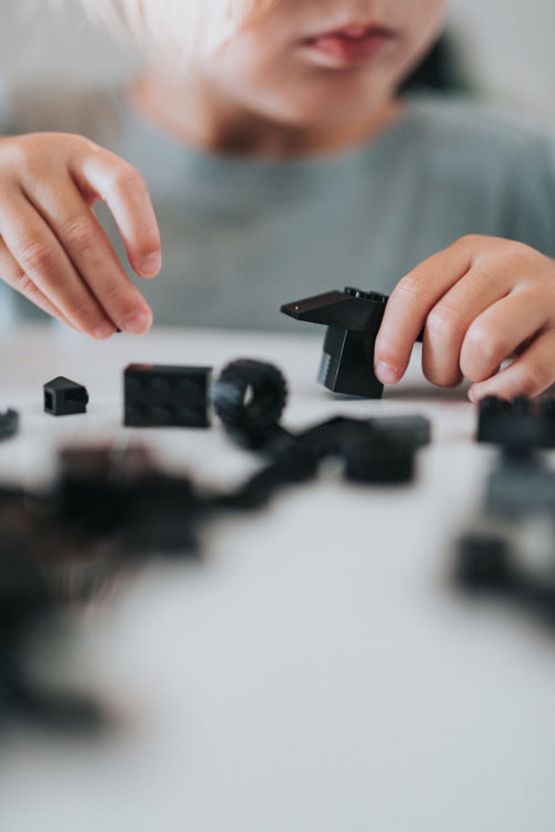 Small white child playing with black legos on a table.