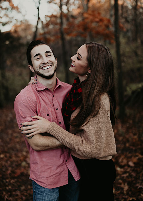 Man in pink shirt happily hugging woman in tan sweater with a fall background