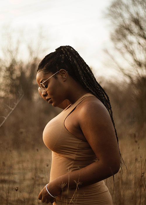 Black woman wearing glasses looking pensive with a backdrop of winter woods